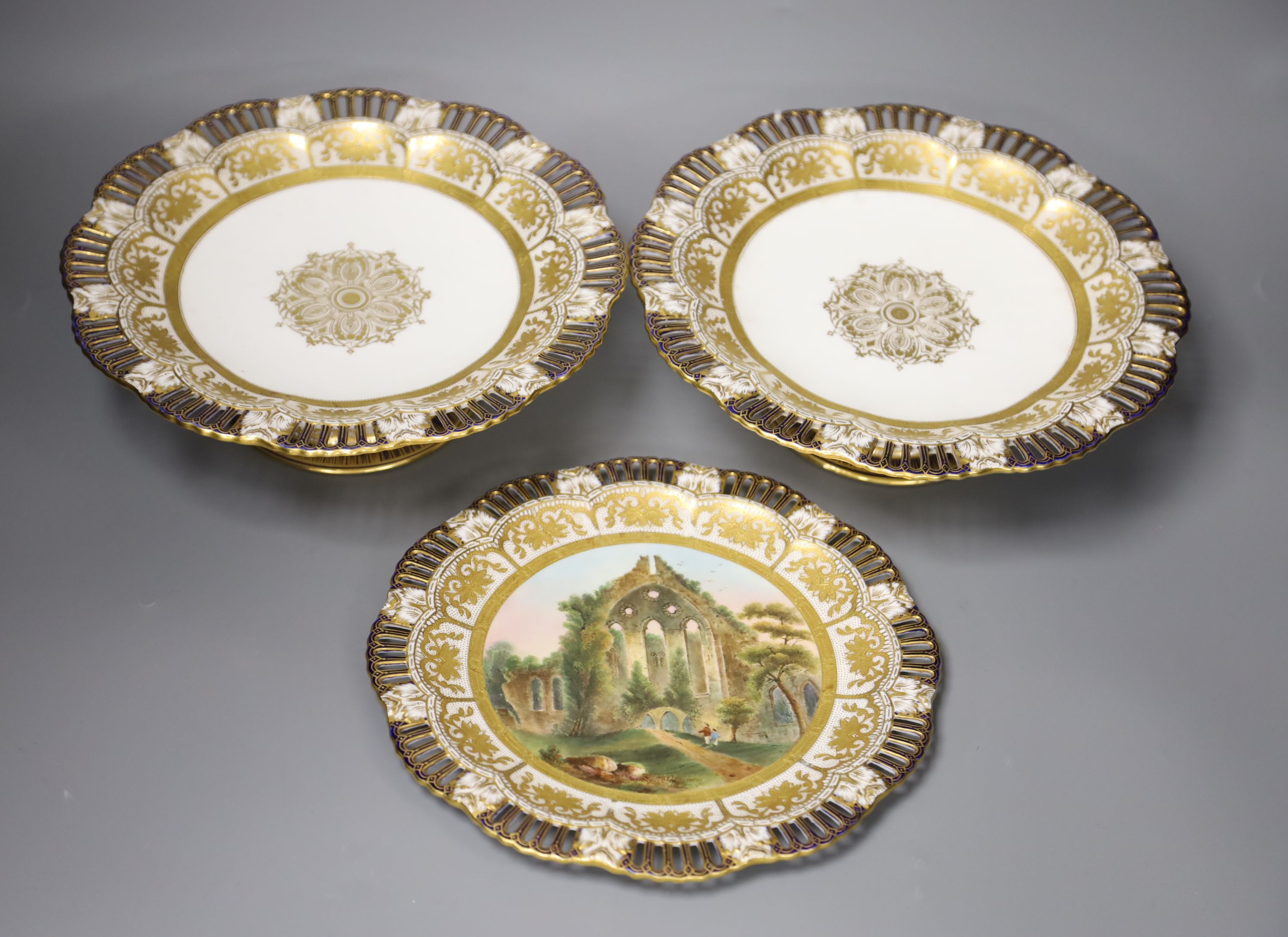A Coalport plate painted with a titled landscape, diameter 23.5cm, and two comport ensuite all have pierced borders, mark Coalport AD17